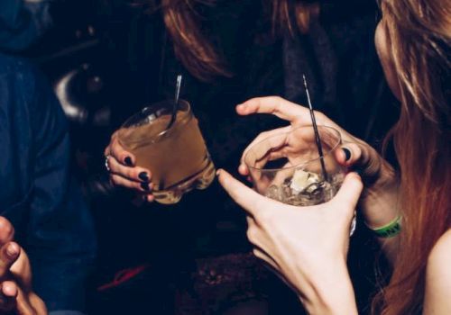 People are enjoying drinks and laughing in a social setting, holding cocktails with straws, showing a lively and relaxed atmosphere.