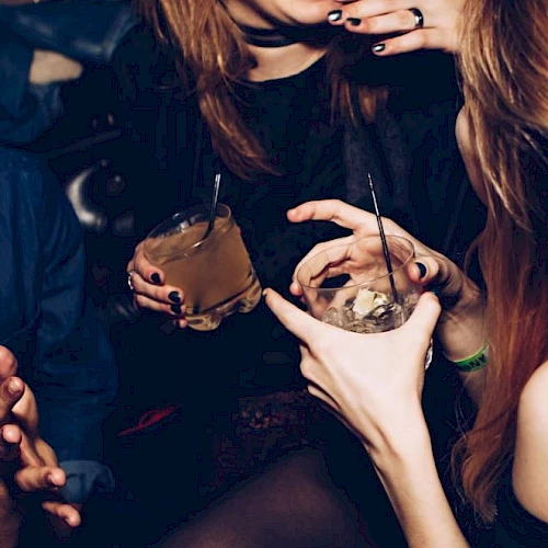 People are enjoying drinks and laughing in a social setting, holding cocktails with straws, showing a lively and relaxed atmosphere.