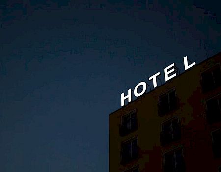 A building at night with illuminated letters spelling "HOTEL" on the roof against a dark sky.