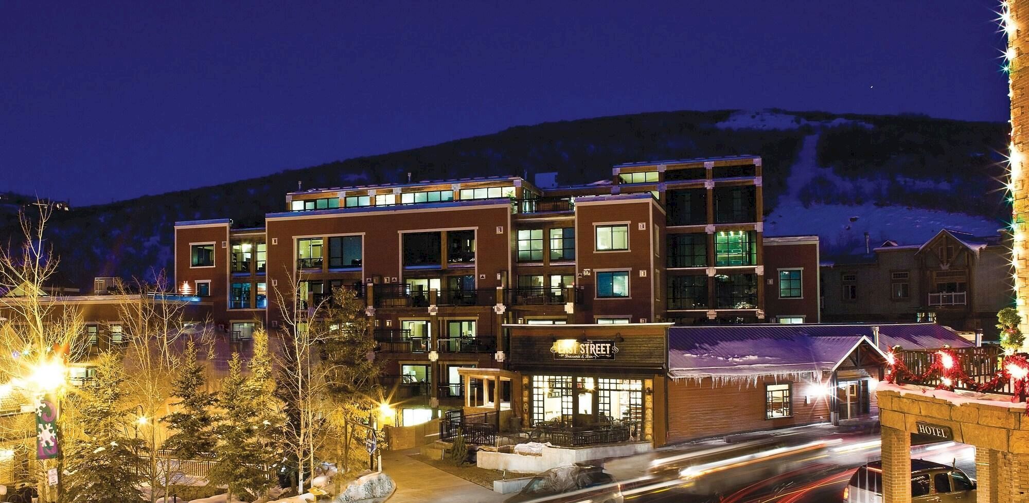 An illuminated building at night with trees and mountains in the background, creating a cozy winter scene.