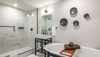 A modern bathroom with a glass-enclosed shower, a freestanding tub, and a black metal vanity; black circular wall decor adds style.