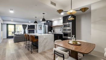 A modern open-concept kitchen and living area with a dining table, stylish lighting, and a marble island.