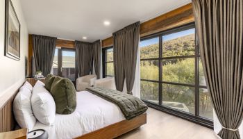 A modern bedroom with a large bed, green pillows, curtain-covered windows, and a scenic outdoor view.