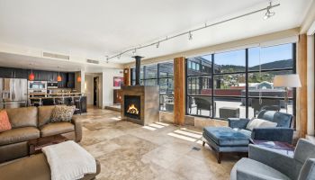 A spacious living area with modern furniture, a fireplace, large windows, and a view of the outdoors and mountains.