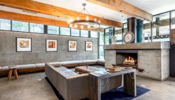 A modern living room with a fireplace, gray sofas, wooden accents, framed artwork, and large windows for natural light.