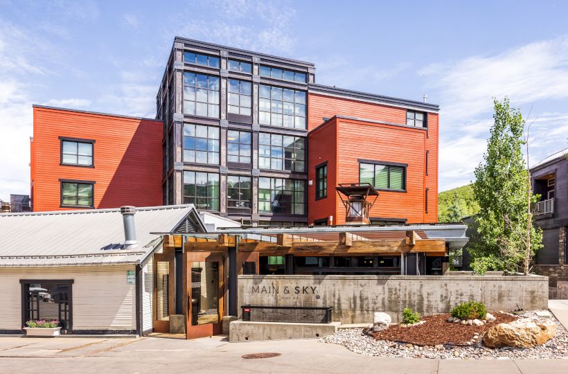 A modern building with red and glass sections, surrounded by trees and a garden, with the label 