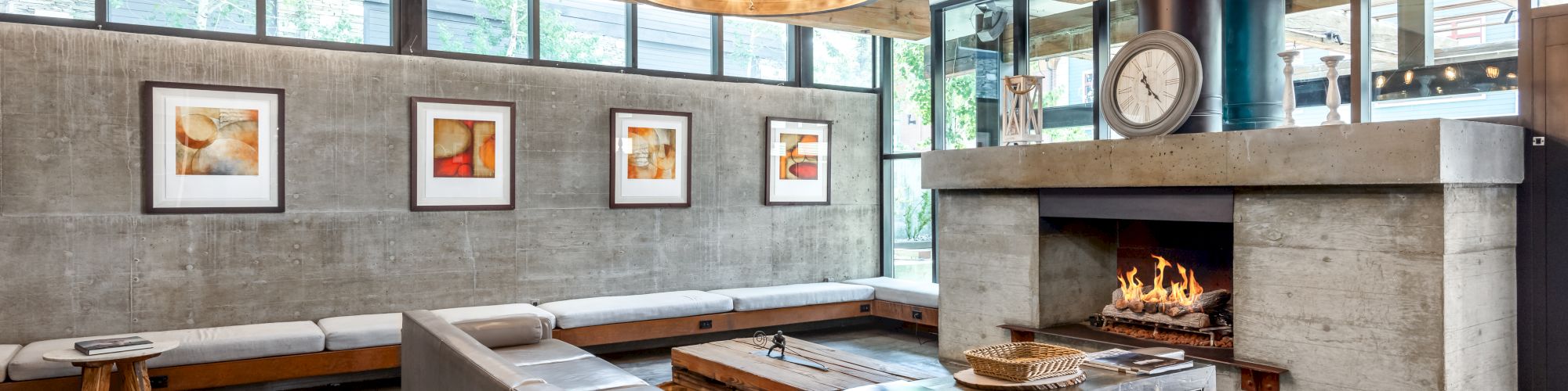 A modern living room with concrete walls, a large chandelier, a fireplace, and a sectional sofa, featuring framed artwork on the wall.