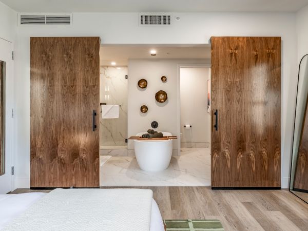 Open wooden doors reveal a modern bathroom with a freestanding white tub, marble walls, and decorative wall bowls.