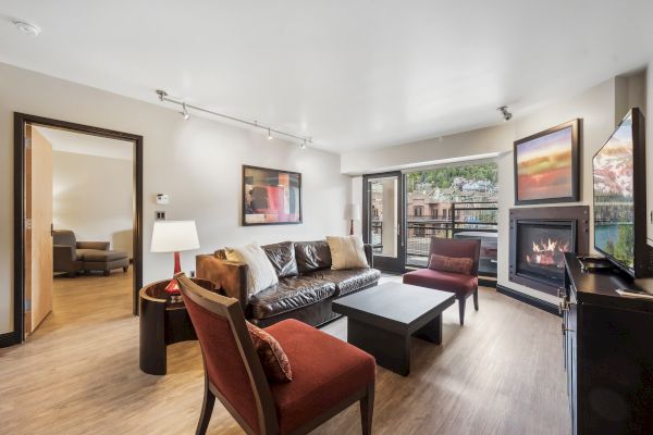 A modern living room with a sofa, chairs, coffee table, fireplace, and large windows offering a scenic view.