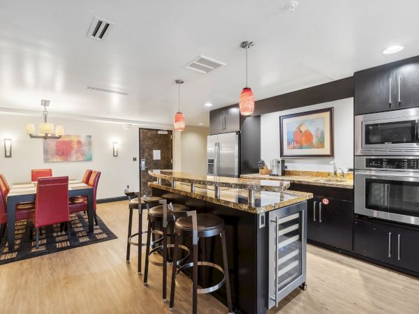Modern kitchen and dining area with granite countertops, bar stools, red dining chairs, stainless steel appliances, and artwork on the wall.