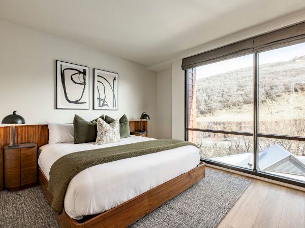 Modern bedroom with a large bed, framed abstract art, and big windows overlooking snowy hills.