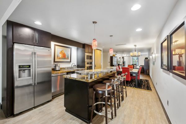 A modern kitchen with stainless steel appliances, a long island with bar stools, and pendant lighting over the counter.