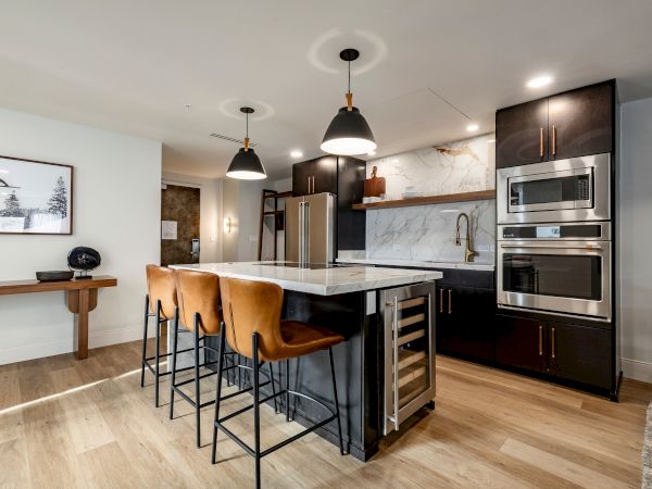 Modern kitchen with a marble island, pendant lights, stainless appliances, dark cabinets, and a marble backsplash, finished with bar stools.
