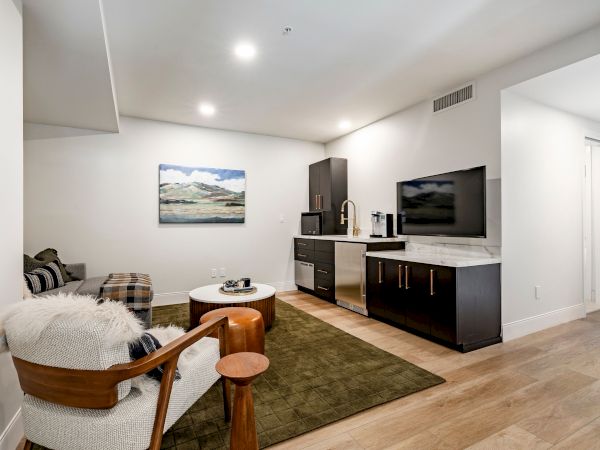 A modern living room with a sectional seating area, a flat-screen TV, and a built-in kitchenette with bar stools.