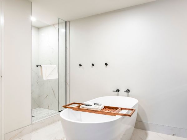 Modern bathroom with a freestanding white tub, glass shower door, and chrome fixtures on a white marble wall.