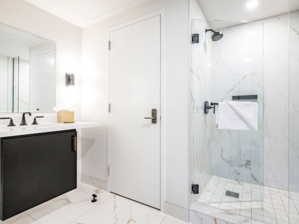 Bright modern bathroom with marble tiles, a glass shower, showerhead, toilet paper, and a sleek vanity with faucets.