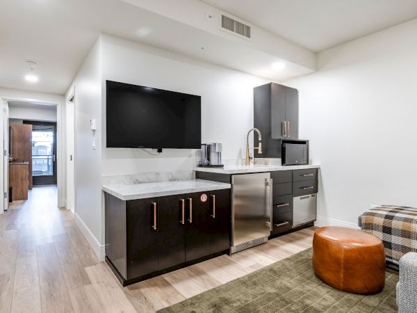 Modern kitchenette with a wall-mounted TV, stainless sink, countertops, and appliances in a bright minimalist living area.
