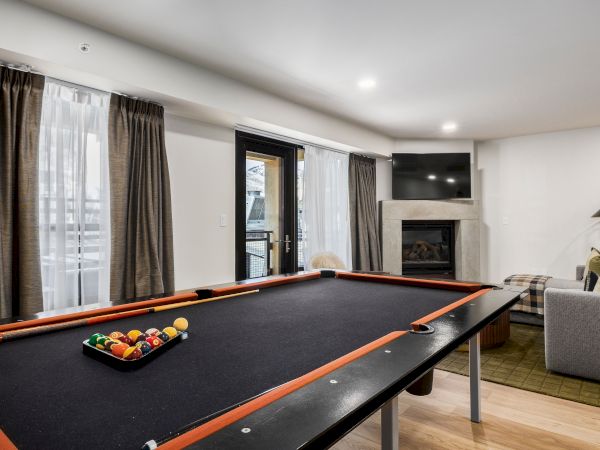 A modern living room with a billiards table, fireplace, wall-mounted TV, and curtains and lamps.