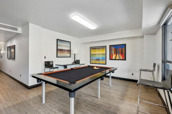 A room with a pool table, abstract art on the walls, chairs, and bright overhead lighting.