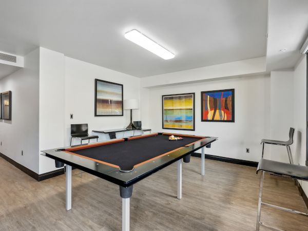 A room with a pool table, abstract art on the walls, chairs, and bright overhead lighting.
