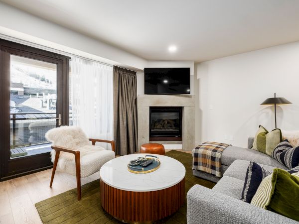 A cozy living room with a stone fireplace, wall-mounted TV, sofa, and large window.