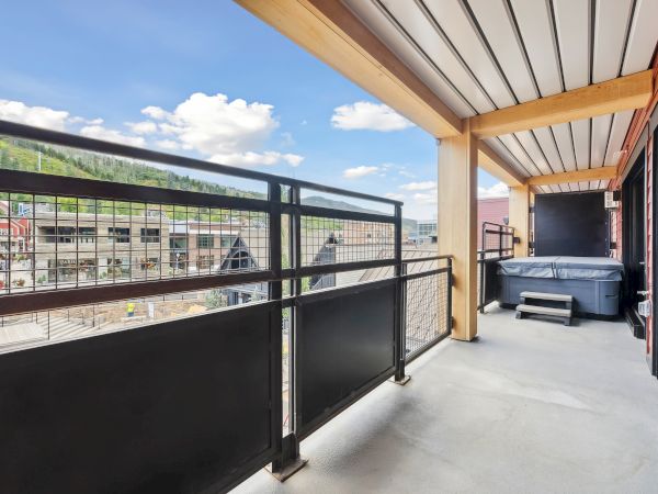 A balcony with mountain views, metal railing, and a hot tub. Bright sky with clouds enhances the scenic beauty of the spot.