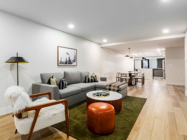 Bright modern living room with gray sectional, rug, coffee table, pendant lights, and dining area beyond.