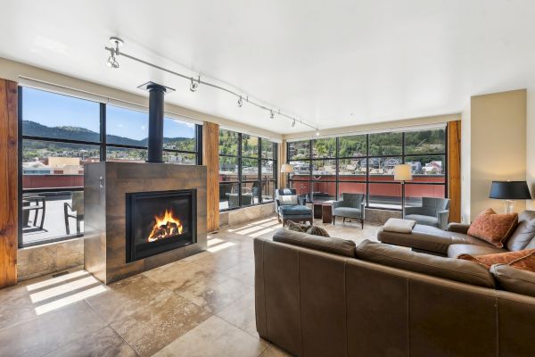 A modern living room with a fireplace, large windows, brown leather sofas, and mountain views.