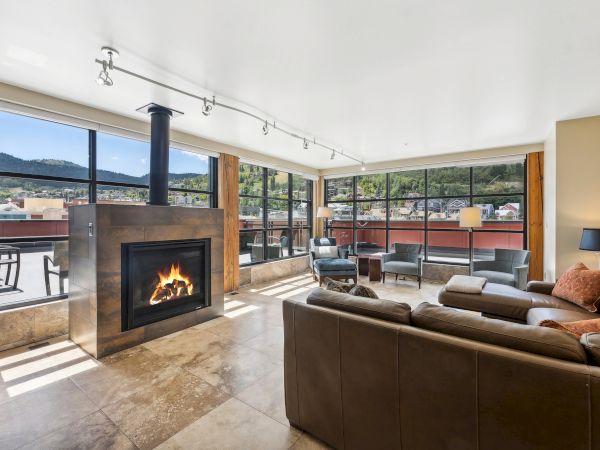 A modern living room with a fireplace, large windows, brown leather sofas, and mountain views.