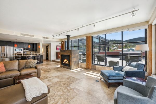 A modern, spacious living area with a fireplace, large windows, and an open kitchen, featuring contemporary furniture and decor.