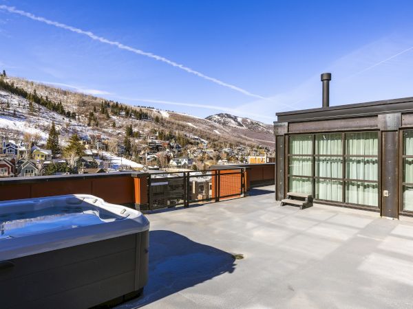 A snowy mountain town view from a patio with a blue hot tub and a glass-walled building under a clear blue sky.