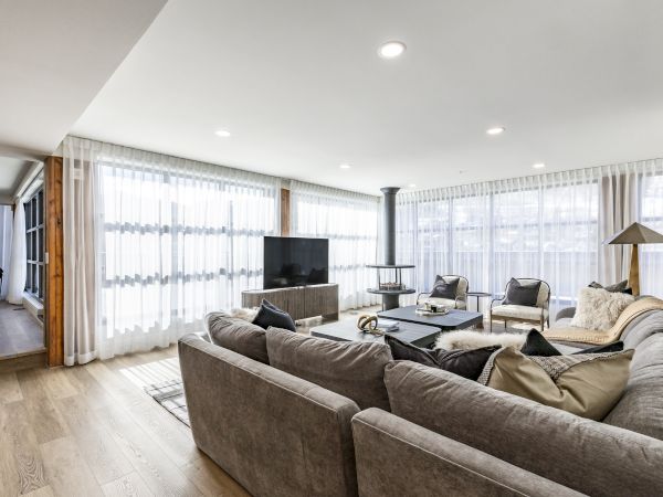 Bright modern living room with gray sofas, a TV on a console, a coffee table, and floor-to-ceiling white curtains.