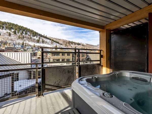 An outdoor hot tub on a balcony, looking over a snowy hillside town with pine trees and houses.
