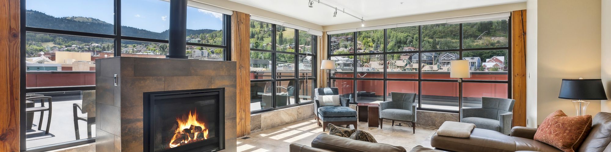 A modern living room features a fireplace, leather sofas, and large windows with scenic views of mountains and a terrace outside.