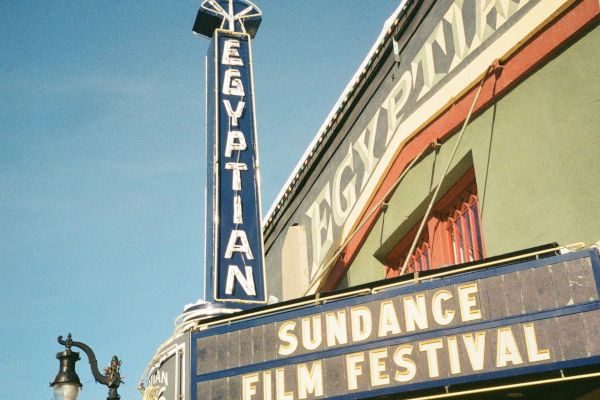 The image shows the Egyptian Theatre with a marquee sign advertising the Sundance Film Festival against a clear blue sky.