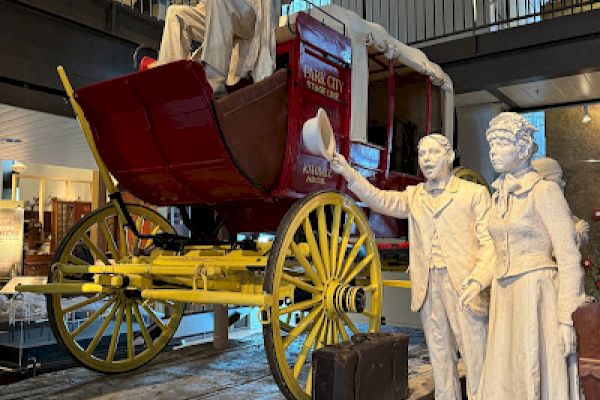 A historic stagecoach display with mannequin figures in period attire, set in a museum setting with a high ceiling and balcony.