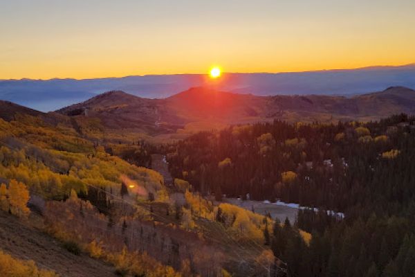 A picturesque sunset over a mountain landscape with autumn foliage and a vibrant sun in the sky.