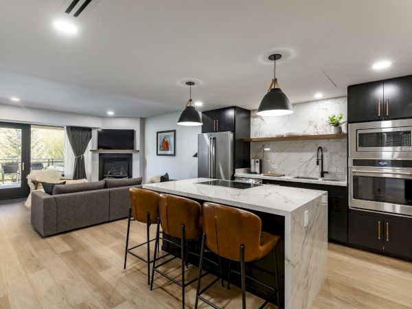 A modern kitchen and living area with a marble island, black cabinets, stainless steel appliances, and a cozy seating area.