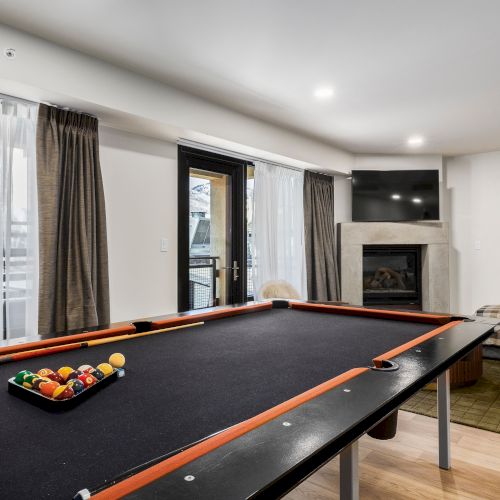 A cozy game room with a full-size billiards table, pool balls, curtains, a TV, and a stone fireplace for lounging.
