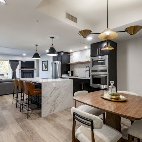 Modern open-plan kitchen and dining area with a marble island, barstools, wooden dining table, and pendant lighting.