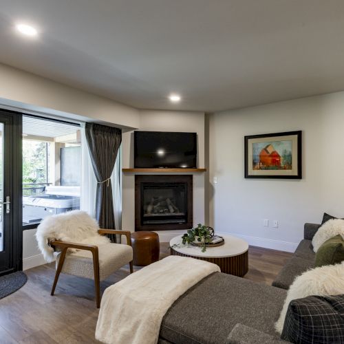 A cozy living room with a fireplace, TV, sofa, chair, and a door leading to an outdoor patio with seating, seen in natural light.
