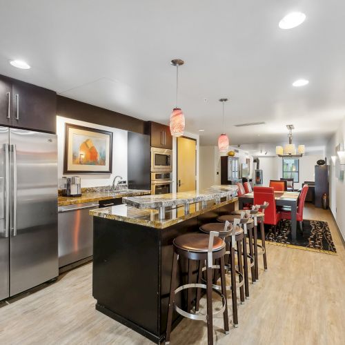 Modern kitchen with stainless steel appliances, a long island with bar stools, pendant lights, and a view of the dining area.