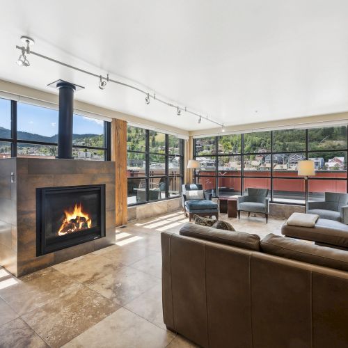 A modern living room features a fireplace, large windows with mountain views, and comfortable seating, creating a cozy atmosphere.