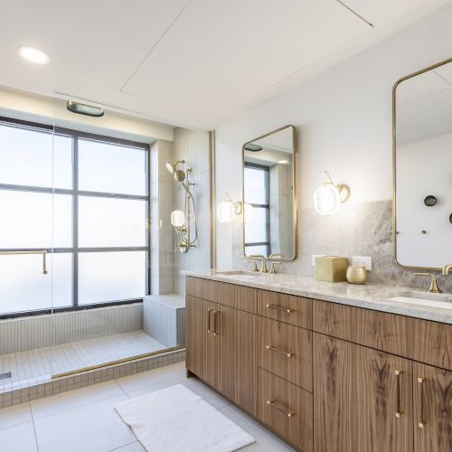 Modern bathroom with a glass shower, double vanity, golden fixtures, and round stone wall art.