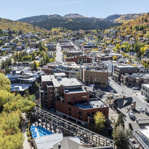 This aerial image shows a town nestled in a valley with buildings and roads, surrounded by hills with autumn foliage.