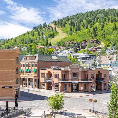 A scenic town with brick buildings, surrounded by lush green hills under a blue sky with scattered clouds.