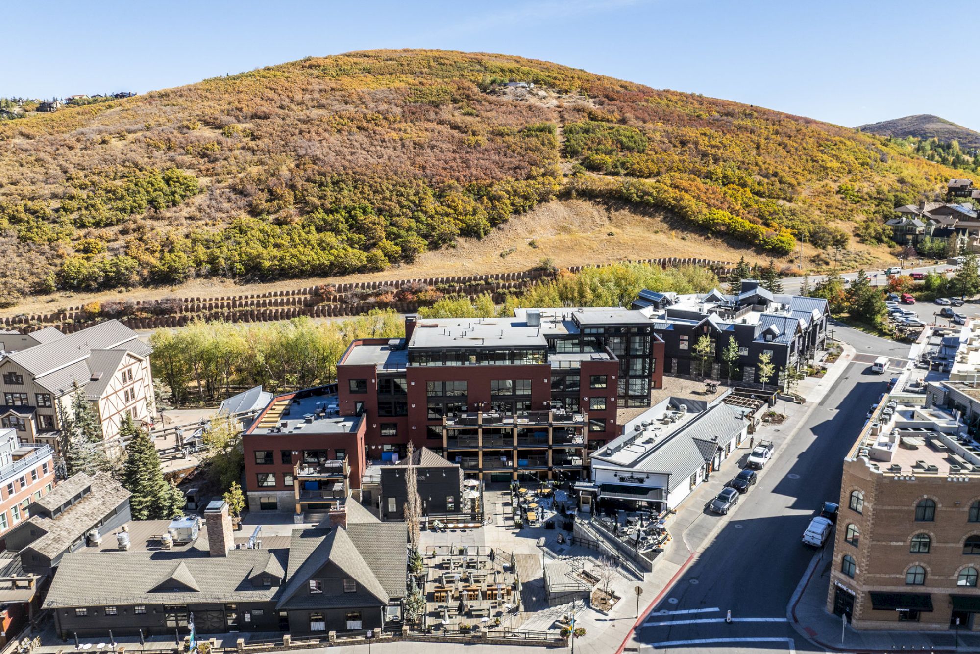 An aerial view of a small town with buildings surrounded by a hilly landscape with autumn foliage under a clear sky.