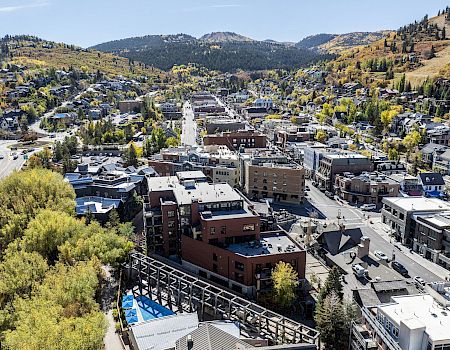 Aerial view of a town in a valley, with a mix of residential and commercial buildings, tree-lined streets, and hills in the background.