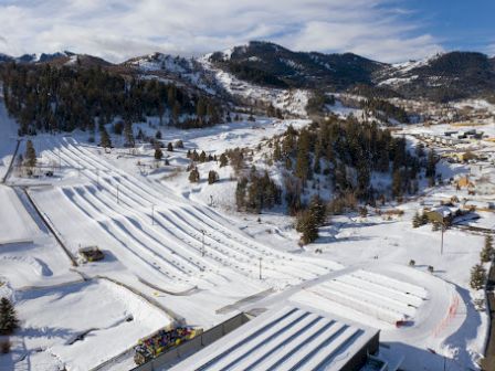 Ski resort with snow-covered slopes, chair lifts, and buildings nestled in a mountainous area, sunny sky, and a winding road nearby, end.