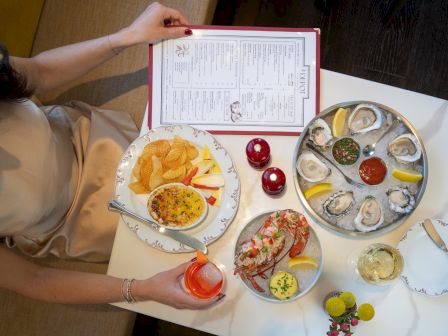 A top-down view of a table with a person dining: oysters on a platter, potato chips, dip, small salads, lemon wedges, drinks, and a menu.